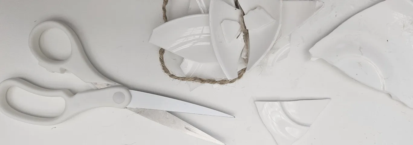 a pair of white handled scissors, shards of broken ceramic and a length of twine