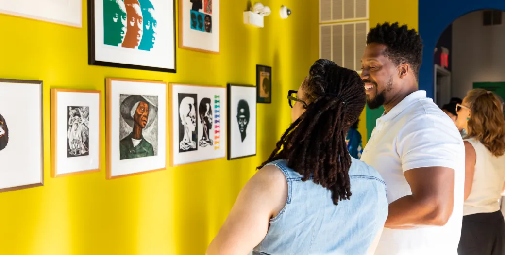 "a woman and man viewing artwork on a yellow wall"