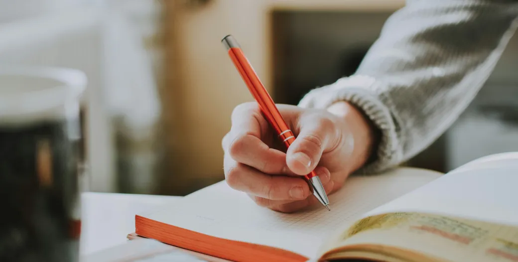 image of hand holding pen over notebook