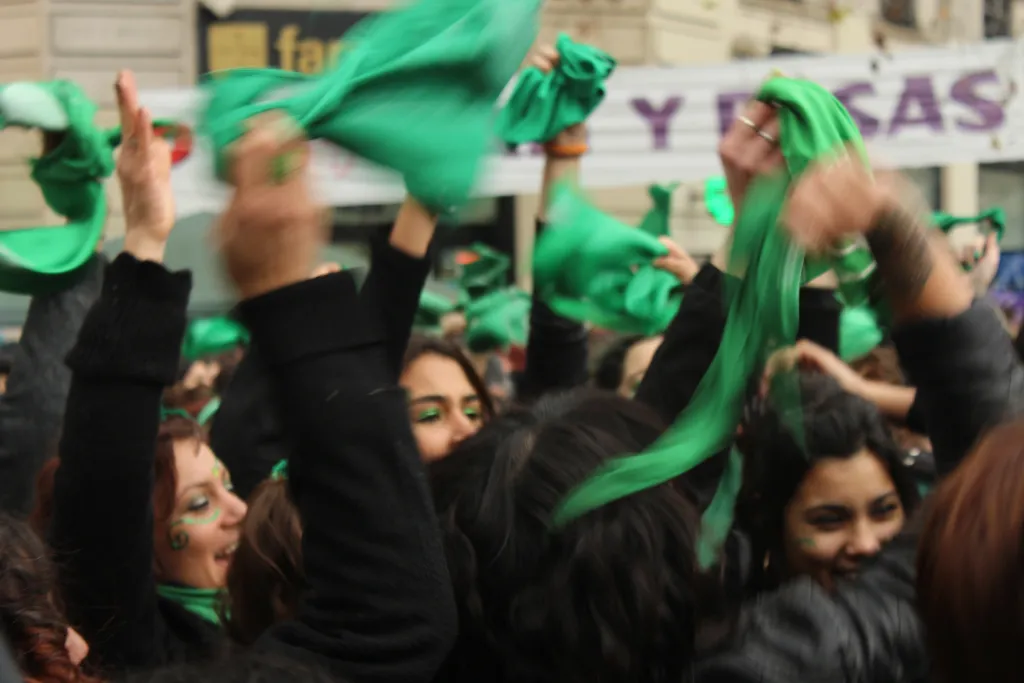 "Photo of a crowd of women waving green bandanas"